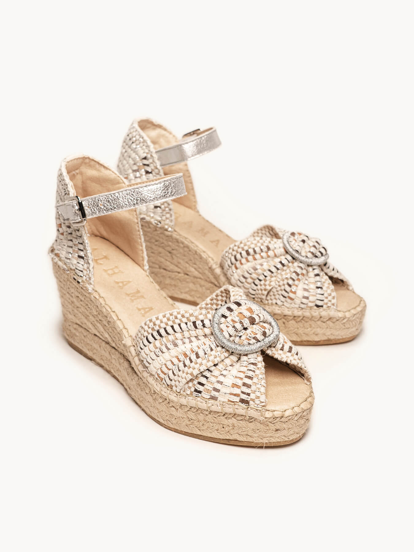 Pair of silver wedge sandals with jute sole on a white background