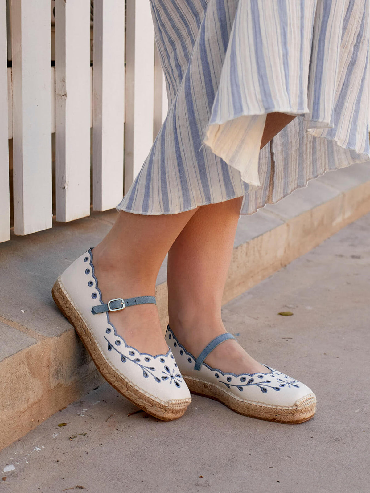 Person wearing white espadrilles with blue accents on the sidewalk