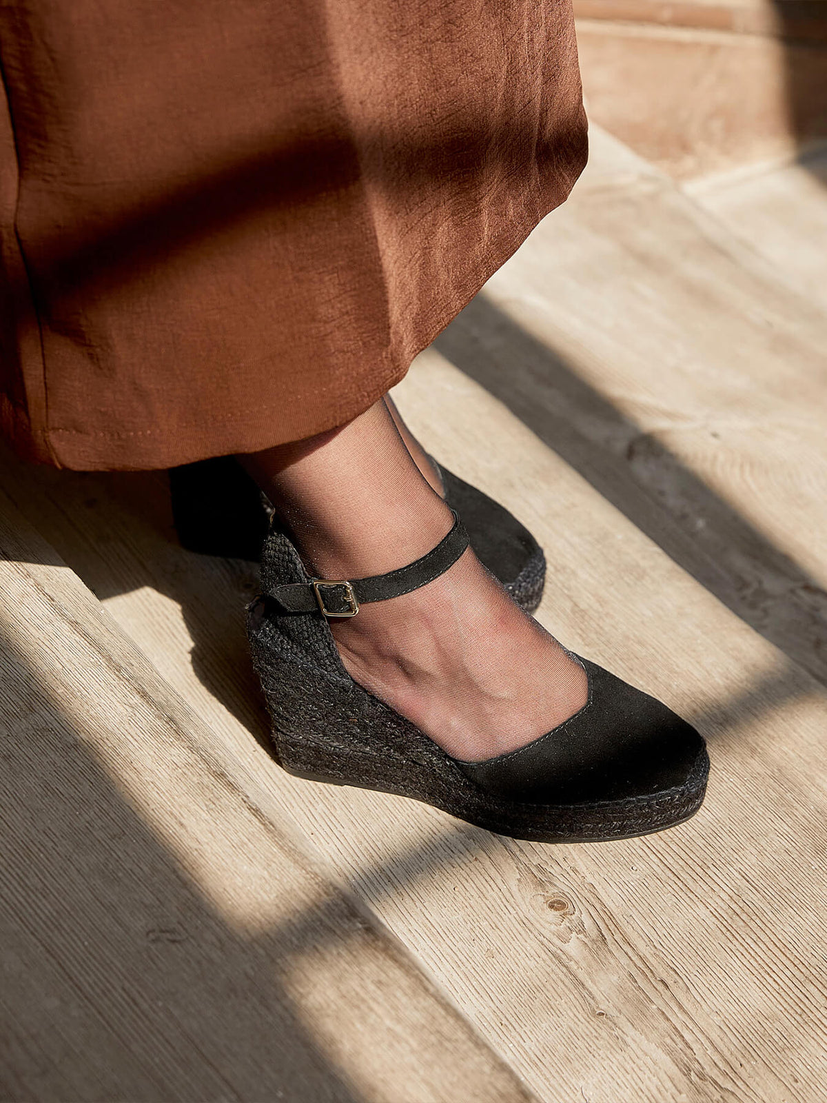 Person wearing black wedge sandals on a wooden floor