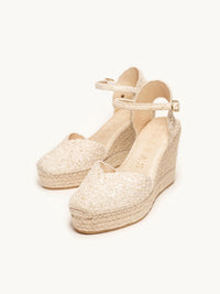 Pair of beige wedge sandals with espadrille sole on a white background