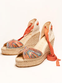 Pair of espadrille wedge sandals with orange straps on a white background