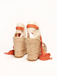Woven wedge sandals with orange straps on a white background