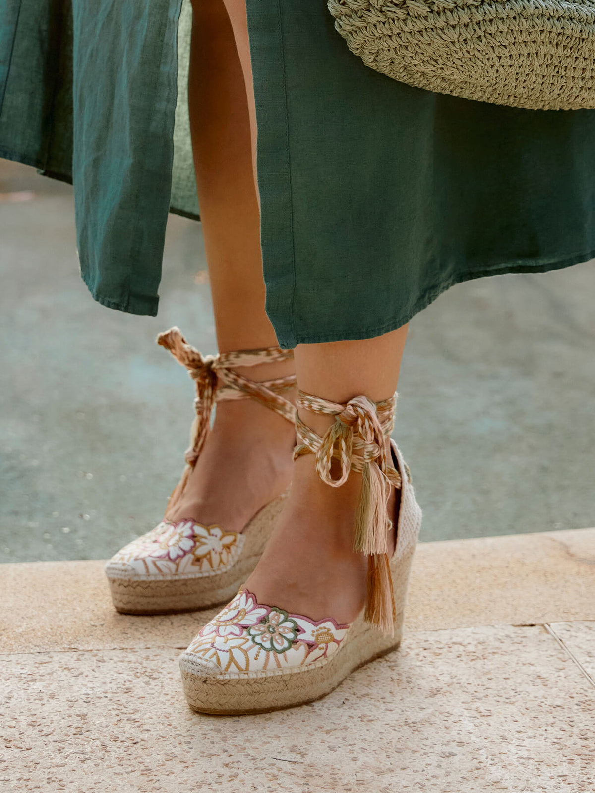 Person wearing floral espadrille wedge sandals with a green skirt and straw bag.