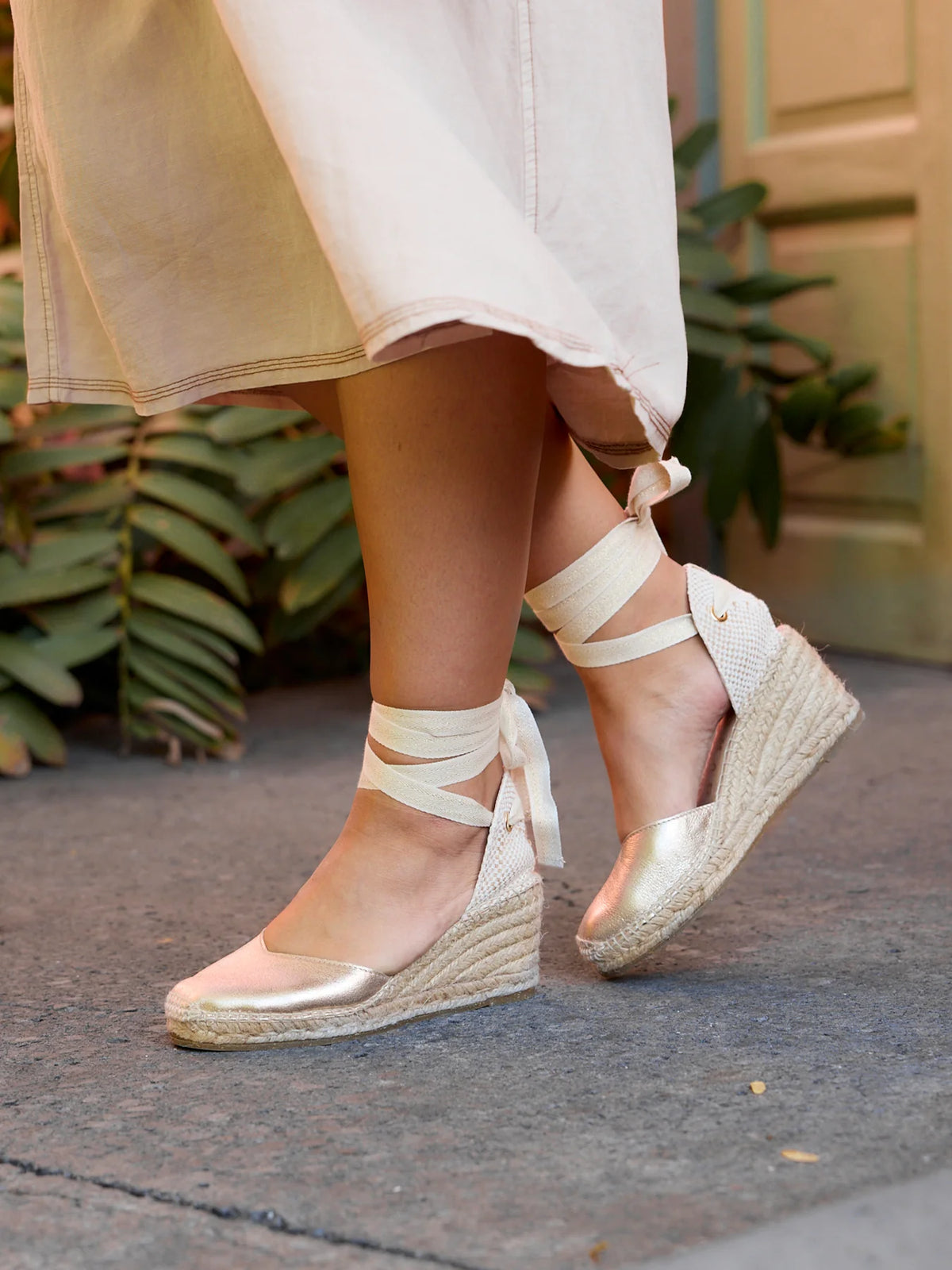 Person wearing white strappy sandals with gold accents on a sidewalk