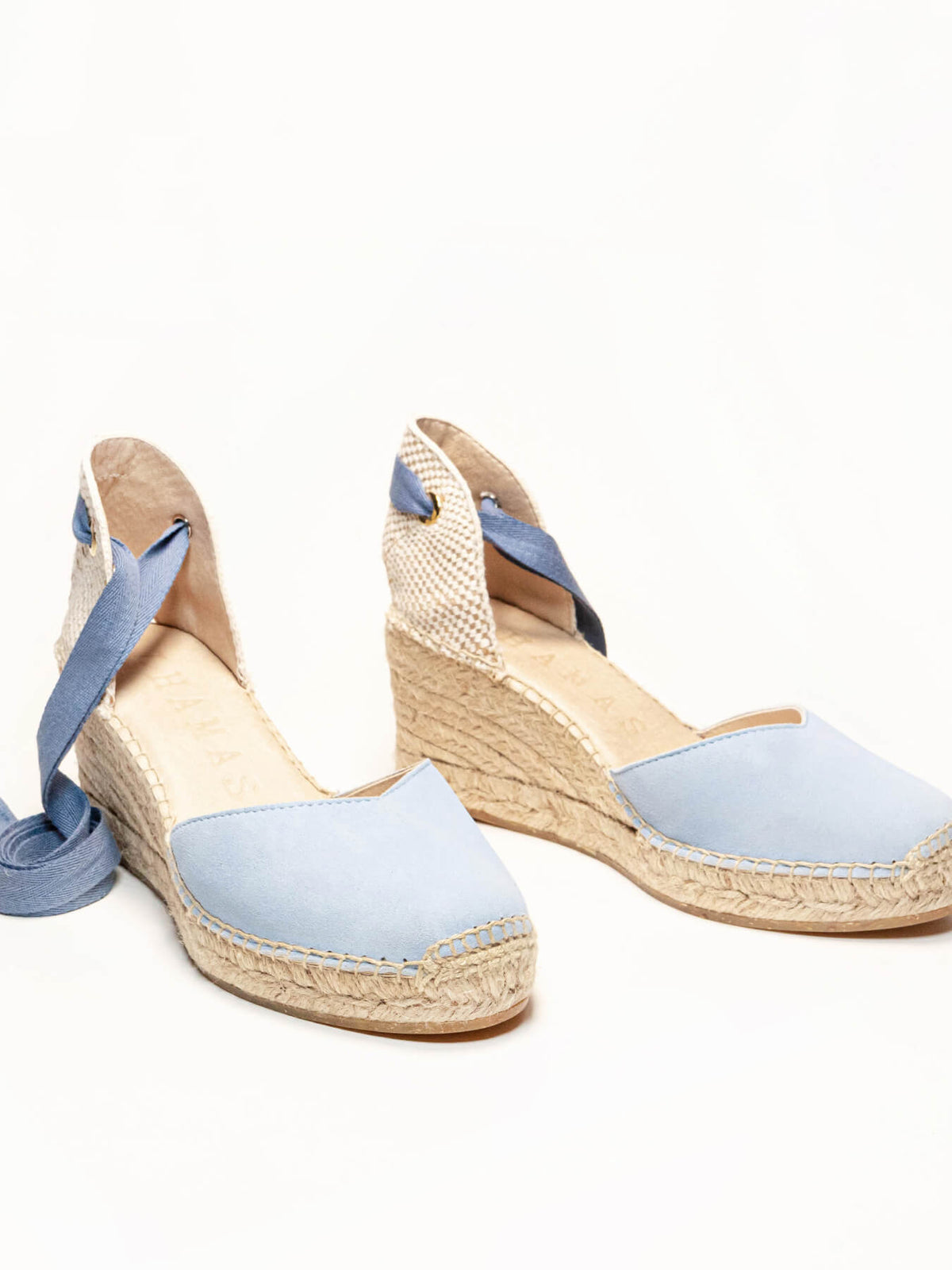 Pair of light blue wedge sandals with espadrille soles on a white background