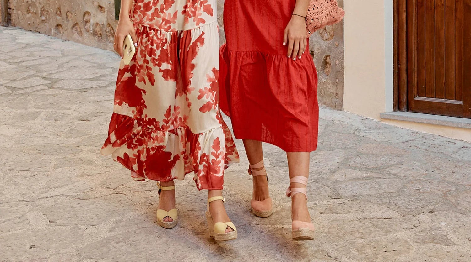 Two women in colorful dresses walking on a stone pavement wearing espadrille sandals